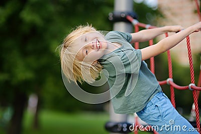 Cute perky preschooler boy having fun on outdoor playground. Spring or summer or autumn active sport leisure for kids. Outdoor Stock Photo