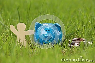 Cute piggy bank, wooden person and jar with coins on green grass Stock Photo