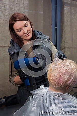 Cute and pleasant brunette, adult girl, European hairdresser, in the process of work, dries the hair of a client in a barbershop Stock Photo