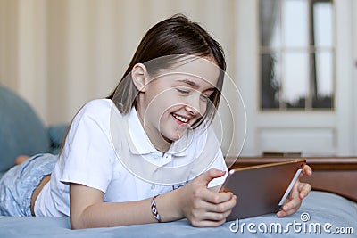 Cute preteen girl smile lying on sofa looking at digital tablet pad Stock Photo