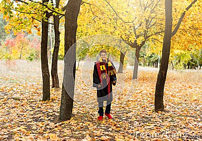 Cute pretty boy in costume of Harry Potter and scarf plays as a magician, reads book in autumn Editorial Stock Photo