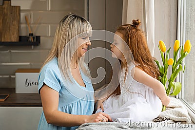 Cute red-haired girl gives yellow tulips to her mom. Mother`s day surprise. Stock Photo