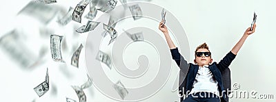 A cute, rich boy with glasses holds dollars and knows how to make money against the background of falling banknotes. Money rain, Stock Photo