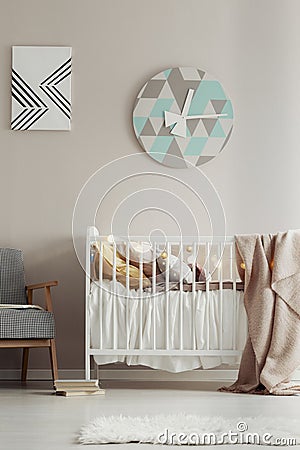 Cute, scandi bedroom interior for a child with a white crib, pastel wall and a round clock. Real photo Stock Photo