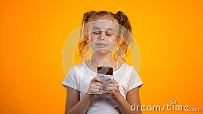 Cute schoolgirl enjoying taste of delicious chocolate, happy childhood, emotions Stock Photo