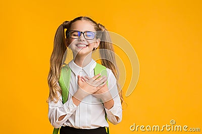 Cute schoolgirl posing putting hands on heart on yellow background Stock Photo