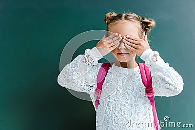 cute schoolkid covering eyes with hands on green . Stock Photo