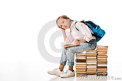 cute schoolkid sitting on books and looking at camera on white. Stock Photo