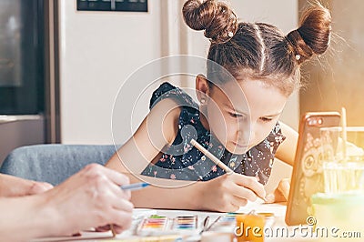 Cute serious Caucasian girl with her mother draws with pencils and paints. Online lessons Stock Photo
