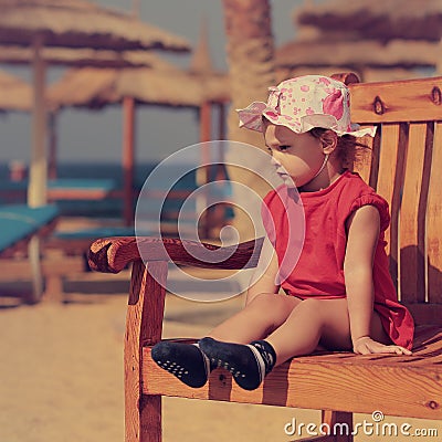 Cute serious kid girl in hat sitting on the bench Stock Photo
