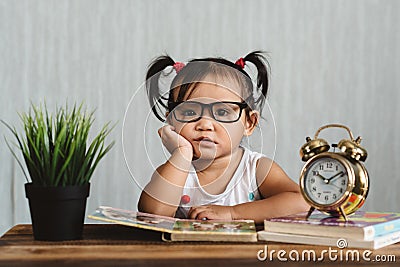 Cute serious looking little asian toddler wearing eyeglasses reading a book on a table Stock Photo