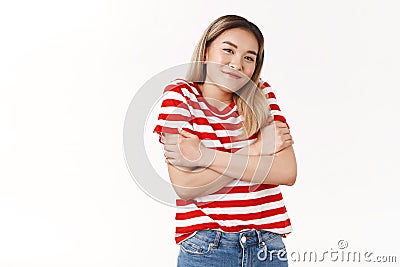 Cute silly asian girl blond haircut wearing summer striped t-shirt shrugging cute smiling cross arms chest feel chilly Stock Photo