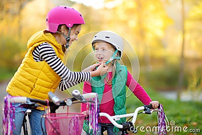 Cute sisters riding bikes in a city park on sunny autumn day. Active family leisure with kids. Children wearing safety hemet while Stock Photo