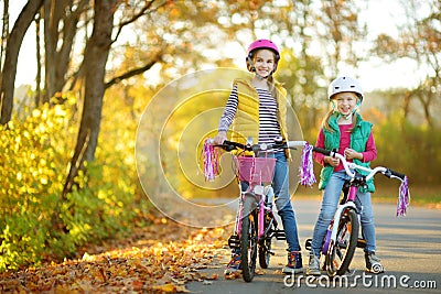 Cute sisters riding bikes in a city park on sunny autumn day. Active family leisure with kids. Children wearing safety hemet while Stock Photo