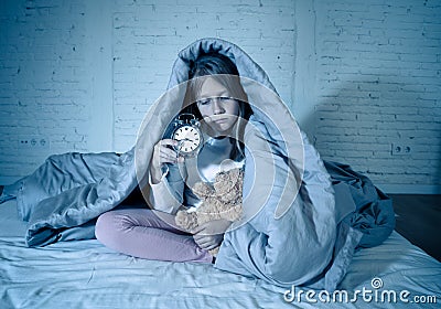 Little girl sitting on bed with teddy bear and alarm clock sleepless at night suffering insomnia Stock Photo