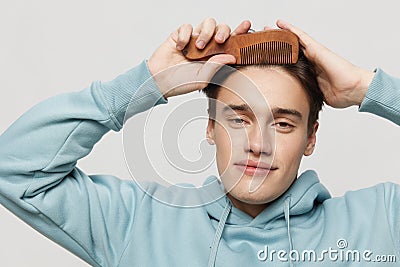 A cute slender young man combs his hair in a light light blue hoodie,with a comb in his hand combing a place in the Stock Photo