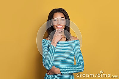 Cute smart mixed race ethnicity black woman in blue shirt thinking on colorful yellow background Stock Photo