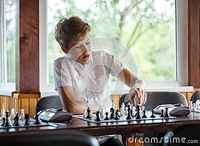 Cute, smart, young boy in white shirt plays chess on the chessboard in the classroom. Education, hobby, training Stock Photo