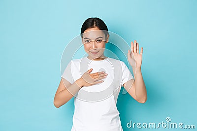 Cute smiling asian girl swearing to tell only truth, making oath or pledge on something. Adorable korean female student Stock Photo