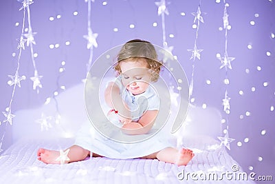 Cute smiling baby girl on bed between beautiful purple lights Stock Photo