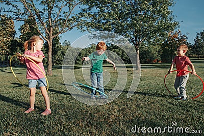 Cute smiling Caucasian preschool girl boys friends playing with hoola hoop in park outside. Kids sport activity. Lifestyle happy Stock Photo