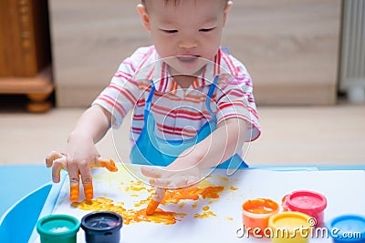 Cute smiling little Asian toddler boy child finger painting with hands and watercolors, kid painting at home Stock Photo