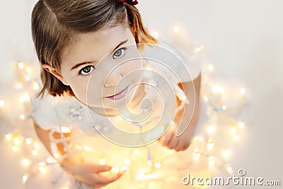 Cute, smiling little girl with glowing Christmas lights Stock Photo