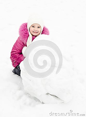 Cute smiling little girl makes snowman in winter day Stock Photo