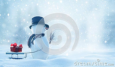 Cute smiling snowman with hat and striped scarf pulling a sled. Winter fairytale.Snowfall in the magic forest.Merry christmas and Stock Photo