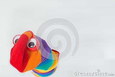 Cute sock puppet with rainbow flag sock, and plastic red eyes. White background, copy space. Fighting for LGBTQ+ rights Stock Photo