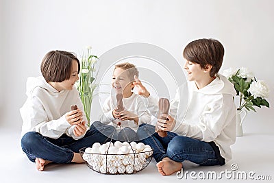 Cute stylish toddler child and older brother, boys with white shirt, playing with eggs and chocolate bunny on Easter decoration Stock Photo