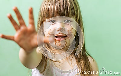 A cute, sweet little girl with chocolate smeared all over her face and fingers. A happy little girl with a dirty face is smiling. Stock Photo