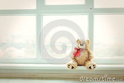 Cute teddy bear at home in white room is sitting near window. Alone bear waiting for a baby boy or girl. Stock Photo