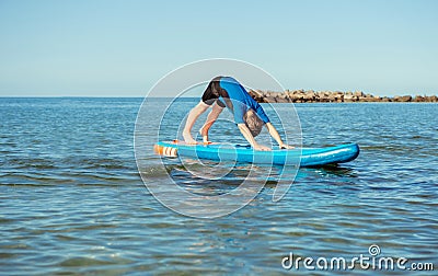 Cute teen boy making yoga on SUP boars in Baltic sea. Stock Photo