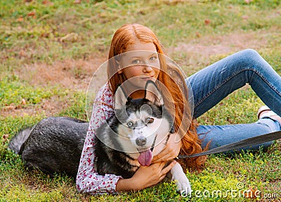 Cute teen girl with red long hair walks with her husky breed dog in the autumn park. Children and dogs. Stock Photo