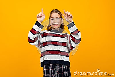 Cute teen girl in a striped casual sweater shows on the wall with copy space Stock Photo