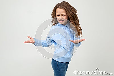 Cute teenage girl in a blue hoodie indignant waving hands on a light gray background Stock Photo