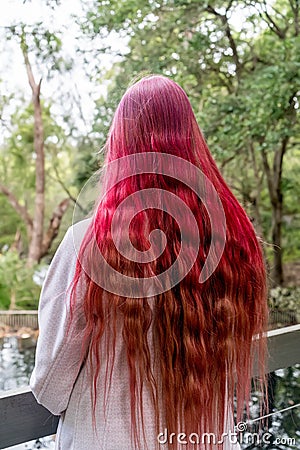 Cute teenage girl with bright raspberry pink ombre long wavy colored hair. Generation Z trends. View from behind Stock Photo