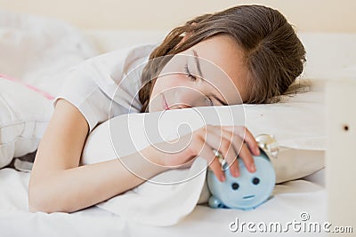 Cute teenage girl holding alarm clock under pillow Stock Photo