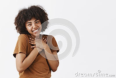 Cute and tender romantic dark-skinned female student with afro hairstyle in brown t-shirt holding hands on heart tilting Stock Photo