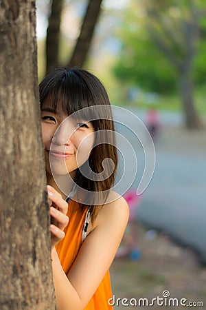 Cute Thai girl hiding behind the tree Stock Photo