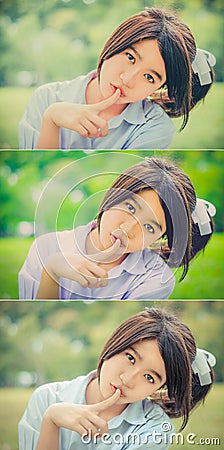 Cute Thai schoolgirl doing hush gesture in green bokeh Stock Photo