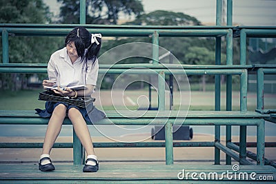 Cute Thai schoolgirl is sitting and reading on a stand in vintage color Stock Photo