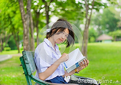 Cute Thai schoolgirl is studying on a bench Stock Photo