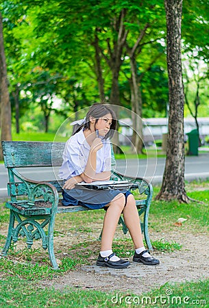 Cute Thai schoolgirl is studying and imagine something on a bench Stock Photo