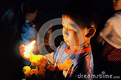 cute theravada buddhist pilgrim kid with a candle and flower float raft during a religious holy celebration Editorial Stock Photo