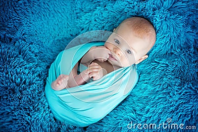 Cute three months old baby boy in blue wrap, lying on a blue blanket, looking curiously Stock Photo