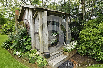 Cute tiny timber antique shack sitting in stunning flower garden Stock Photo