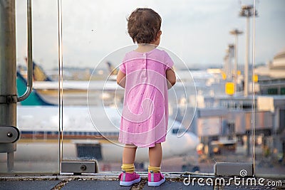 Cute Toddler baby in a pink dress looks at the planes at the airport. Waiting for a flight flight. back view Stock Photo