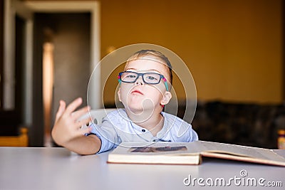 Cute toddler boy with down syndrome with big glasses reading intesting book Stock Photo